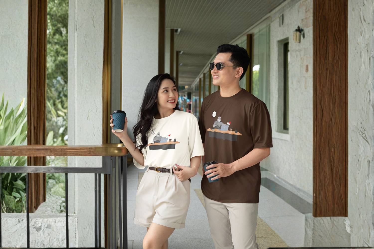 Two people in the Last Minute Task tee, walking a corridor with coffee